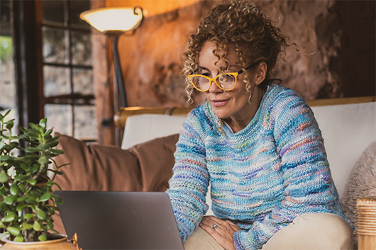 A smiling woman checking the current rates for an APGFCU High Yield checking account on her laptop.